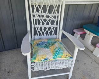 White wicker rocking chair with lattice back and arms, featuring a colorful tropical patterned cushion seat.
