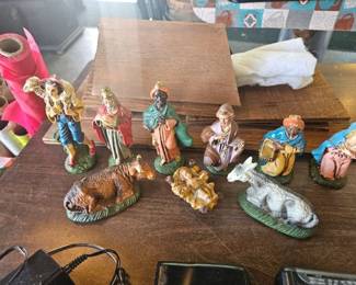Vintage nativity set with painted ceramic figurines including Mary, Joseph, baby Jesus in a manger, three wise men, a donkey, and a lamb displayed on a table.