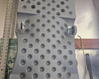Gray metal running board or footplate with multiple raised circular knobs for traction, leaning upright against the wall.