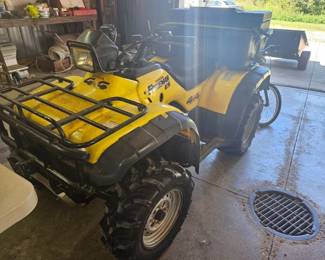 Yellow Honda Foreman all‑terrain vehicle with front and rear cargo racks and large rugged tires, parked indoors.