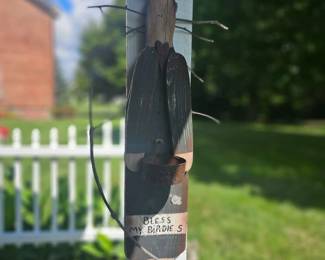Decorative garden stake featuring a rustic metal dragonfly attached to a small sign that reads "Bless the birds", mounted on a white wooden post.