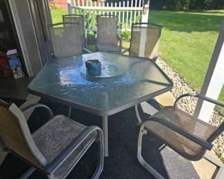 Outdoor patio dining set featuring a square glass-top table and four matching beige sling-back chairs, situated on a covered porch.