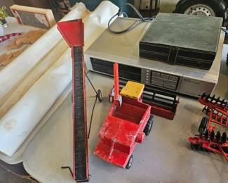 Assorted workshop items including a red-handled clamp or jack, black plastic tool case, long beige boards, and a row of socket bits.