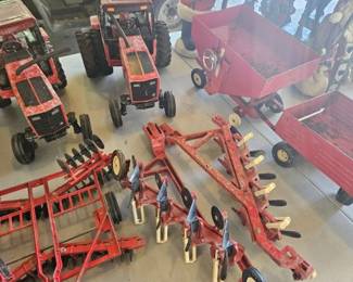 Lot of red toy farm equipment and accessories including toy tractors, wagons, plows, trailers and attachments displayed together.