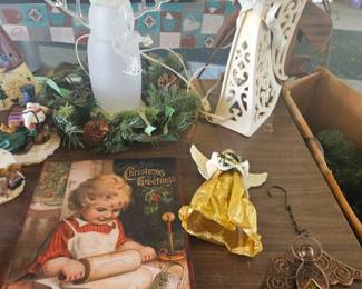 Assorted Christmas ornaments and figurines on display, including an angel candle holder, ceramic angel reading a book, golden bell ornament, a bronze key-shaped cross with "HOPE," and other small decorations.