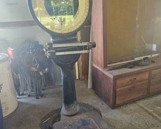 Vintage Toledo industrial platform scale with circular dial and cast iron base, positioned in front of a glass-front display cabinet.