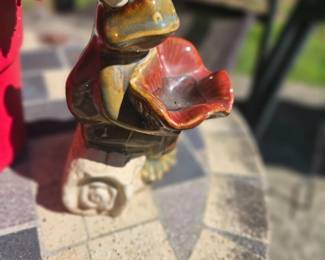Ceramic frog figurine perched on a snail-shaped base holding a red-brown lily-shaped bowl, perfect for a small planter or bird feeder.