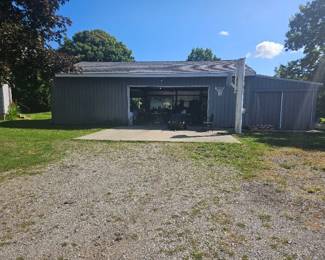 Front view of a large gray barn or garage with metal siding and open doorways, situated at the end of a gravel driveway.