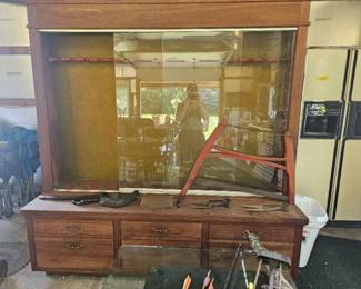 Antique wooden glass display case with multiple drawers, a red metal support bar, and assorted items displayed inside.