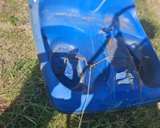 Blue molded plastic kayak hull or paddle boat seat section with foot wells and handles, scuffed and sitting on grass.