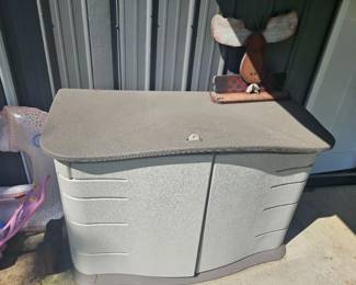 Gray plastic outdoor storage deck box or bench with hinged lid and paneled sides, situated on patio.
