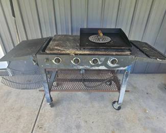 Large outdoor propane grill with multiple burners, side shelves, mesh lower rack, and lid; on wheels.
