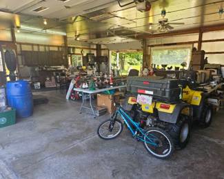 Interior of a barn or workshop featuring a yellow ATV and a small blue bicycle surrounded by tools, workbenches, and storage shelves.