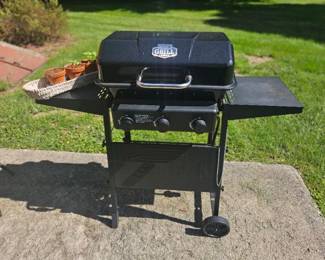 Black Char-Broil outdoor grill on wheels with hinged lid, side shelves and two burner knobs, includes a few small terracotta pots on the side.