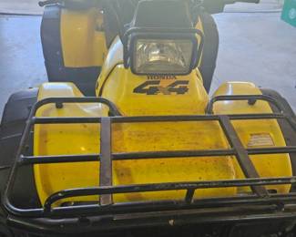Rear view of the yellow ATV showing the large rear cargo rack, black seat and handle bars.