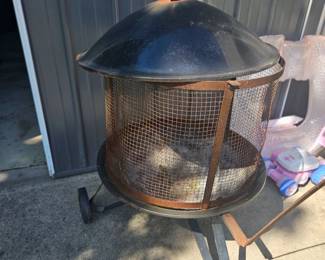 Black metal outdoor fire pit with domed lid and mesh fire screen on a three-legged stand.