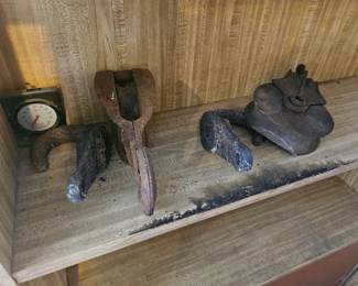 Collection of vintage cast iron clothes irons and other small antique metal items displayed on a wooden shelf.