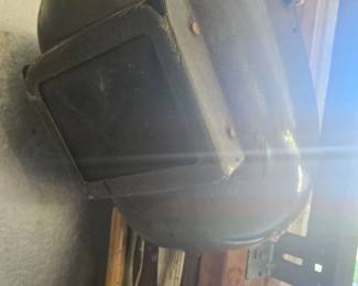Welding helmet or protective face shield with dark visor hanging on a hook against the wall of the barn.