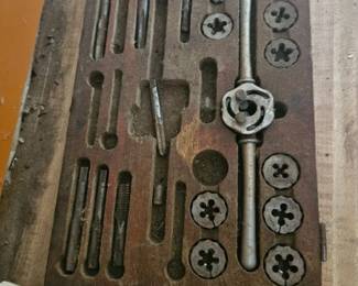 Vintage metal tap and die set with various circular dies and taps arranged on a wooden board.
