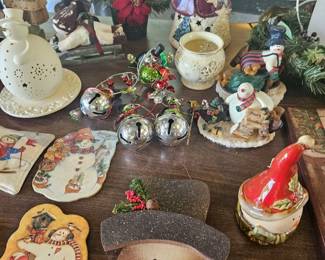 Collection of festive holiday decorations including a Santa head mug, vintage wooden Santa ornaments, cardinal bird figurine, small ceramic angel with candle, and other Christmas-themed decor pieces arranged on a table.