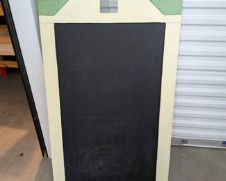 A unique and substantial chalkboard, crafted from durable wood and designed in the shape of a charming house with a green roof and red trim. Perfect for drawing, writing practice, daily messages, or imaginative play in a classroom, homeschool, child's room, or play area. Features a convenient top cutout (like a window) and includes pre-installed tabs for easy wall mounting.
