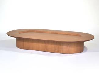 CONTEMPORARY LOW FORM COFFEE TABLE | Ovular low-form coffee table; having slightly recessed central area, solid base, and wood grain finish.
Dimensions: h. 10 x w. 35.25 x l. 63 in