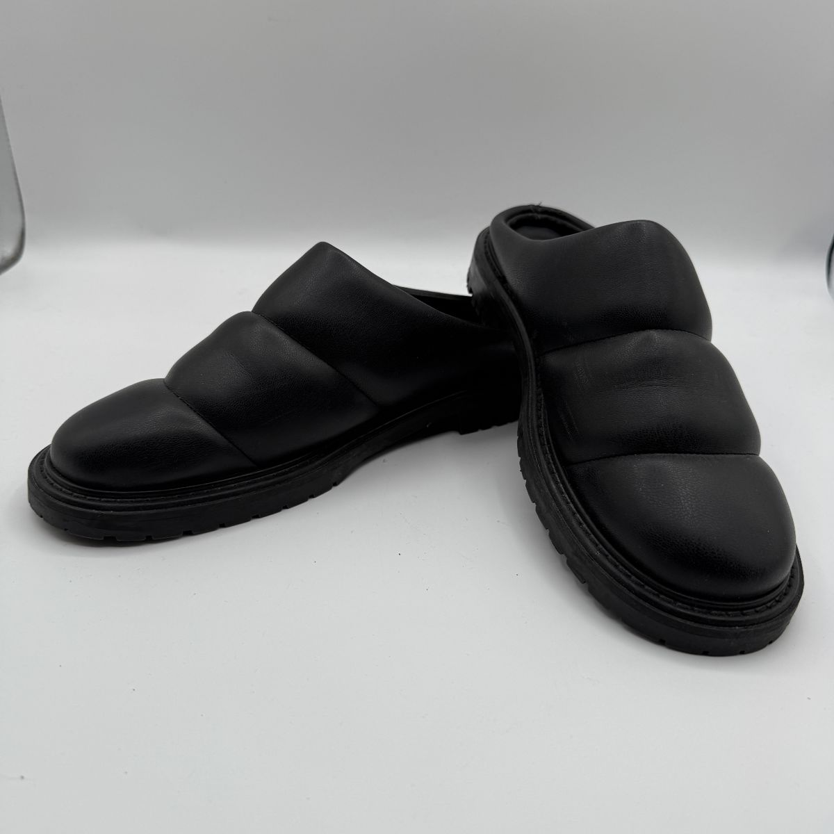 Lot #29 STAUD Black Soft Leather Mules with Chunky Sole Size 38. Black mules featuring a chunky sole, soft leather upper, three pleated bands on the front, and a logo embossed on the bottom reading 'STAUD MADE IN PORTUGAL'. Size 38 indicated on a tag. Beautiful condition with very little to no signs of wear. 
Please see photos and description for condition. Please be prepared with adequate help and vehicle size for furniture, appliances and other bulky items. 