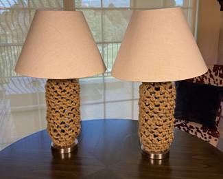 Two table lamps featuring a knotted rope design in a natural beige color. The bases are made of metal with a brushed finish. Each lamp is topped with a conical cream-colored fabric shade.
