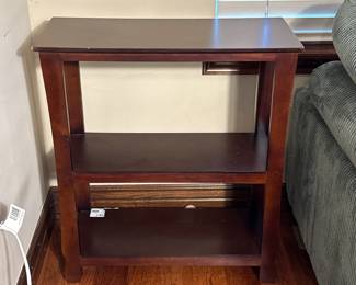 A dark wood finish side table featuring two open shelves. The table has a rectangular top and straight legs, with visible grains in the wood. Measurement tools are placed on the surfaces, indicating its dimensions. There are no visible logos or brand names.