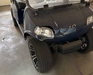 
EVolution Black electric golf cart with a canopy top, featuring two-tone seating in black and gray. The cart has custom black wheels with a stylish design, a steering wheel with a silver center logo, and various dashboard controls. The exterior includes a clear windshield and headlights, with visible wiring inside. Powers on and appears to be in good working order. See photos for front end damage. 