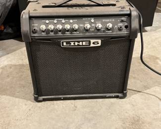 Black amplifier with a textured exterior, featuring a control panel with a variety of knobs and switches. The brand name 'LINE 6' is prominently displayed on the front. The amplifier has a rectangular shape with a mesh speaker cover. There are labels on the rear and sides with specifications and power requirements, including '120V' and '75 W Max.'