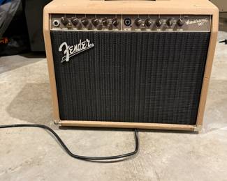 Tan textured exterior with a black speaker grille. Front features the Fender logo and controls for FX SELECT and FX LEVEL. The top right corner displays the text 'Acoustasonic 90'. The rear includes inputs for footswitch, balanced line out, and aux, along with various warning labels. Serial number visible on the backside.