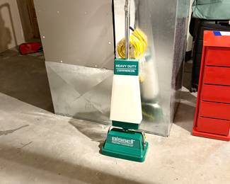 This floor care machine features a green base with a white upper section. It is branded with 'Bissell' and 'BigGreen Commercial'. The machine includes a long handle and comes with multiple brush accessories in white, brown, and yellow colors. Additionally, a metal plate on the machine displays the model 'P-2100' and series number '72-131K'.
