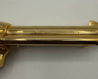 A gold-plated .22 Colt Collectible revolver featuring a pearl-colored grip. The gun has a shiny, metallic finish with a distinct shape, showcasing ornate detailing. Engraved text on the barrel reads '1864-1964 KANSAS SERIES WICHITA-1984.' The grip has a gold emblem and the overall design is a classic revolver style.