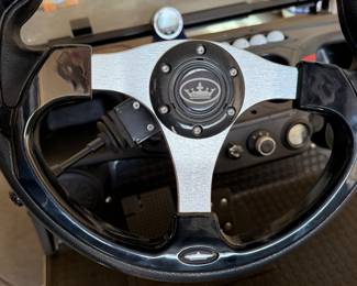 
EVolution Black electric golf cart with a canopy top, featuring two-tone seating in black and gray. The cart has custom black wheels with a stylish design, a steering wheel with a silver center logo, and various dashboard controls. The exterior includes a clear windshield and headlights, with visible wiring inside. Powers on and appears to be in good working order. See photos for front end damage. 