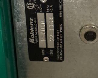 This floor care machine features a green base with a white upper section. It is branded with 'Bissell' and 'BigGreen Commercial'. The machine includes a long handle and comes with multiple brush accessories in white, brown, and yellow colors. Additionally, a metal plate on the machine displays the model 'P-2100' and series number '72-131K'.
