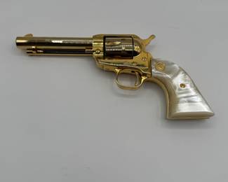 A gold-plated .22 Colt Collectible revolver featuring a pearl-colored grip. The gun has a shiny, metallic finish with a distinct shape, showcasing ornate detailing. Engraved text on the barrel reads '1864-1964 KANSAS SERIES WICHITA-1984.' The grip has a gold emblem and the overall design is a classic revolver style.