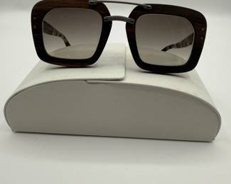 Signature Prada Style! Oversized square sunglasses featuring a dark wooden frame. The lenses are gradient and tinted, transitioning from dark to light. The temples are made of a tortoiseshell pattern, with the brand name 'PRADA' elegantly displayed. The sunglasses are accompanied by a white case.