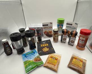 Assorted spice jars and seasoning packets including various colors like brown, red, and tan. Features brands like Urban Accents, McCormick, and Hidden Valley. Packaging displays logos and text such as 'DryGlaze', 'Street Corn', 'Chili Seasoning', and 'Sea Salt Grinder'. Includes glass and plastic containers, with some being transparent. Notable items include ginger and chili powders in resealable bags, along with two clear spice grinders.