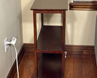 A dark wood finish side table featuring two open shelves. The table has a rectangular top and straight legs, with visible grains in the wood. Measurement tools are placed on the surfaces, indicating its dimensions. There are no visible logos or brand names.