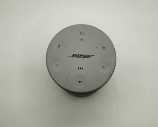 Gray portable smart speaker with a cylindrical shape. Features a perforated speaker grille at the bottom. Top control panel includes buttons for power, Bluetooth, volume, and additional controls. The brand name 'BOSE' is prominently displayed on the top surface.
