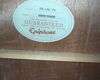 Black acoustic guitar with a glossy finish featuring a sunburst design. It includes colorful decorative stickers of a shield and a deer, positioned on the body. The brand name 'Ibanez' is displayed on the headstock and the label inside the guitar indicates the model AEG20II-TRS-BR-01. The fretboard is made of dark wood with gold tuners, and the guitar is housed in a fitted hard case with a soft interior lining.