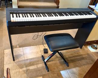A black digital piano featuring a full keyboard with white and black keys. The brand name 'Yamaha' is clearly visible on the front of the piano. The model number 'P-45' is printed on one side. The piano has a sleek design with a sturdy black base. An adjustable black music bench is included, with a rectangular seat and a folding X-frame for support.