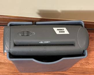 Description:
Gray rectangular paper shredder with a top opening and a label that reads 'PRIVACY GUARD'. The shredder features a control button on the front.
