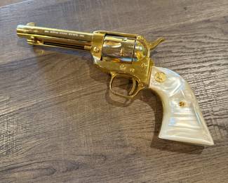 gold-plated .22 Colt Collectible revolver featuring a pearl-colored grip. The gun has a shiny, metallic finish with a distinct shape, showcasing ornate detailing. Engraved text on the barrel reads '1864-1964 KANSAS SERIES WICHITA-1984.' The grip has a gold emblem and the overall design is a classic revolver style.
