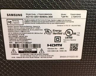Samsung brand monitor, 24 inches in size, black color, LCD display. Features on-screen text indicating device connection issues. Model number LT24H310, with a sleek design and a base stand. Includes an HDMI port for connectivity. The back has a label detailing specifications including model and energy certification.