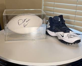 A blue and white Nike football cleat the Autograph of Dalton Risner #66. The cleat has black studs on the sole and a logo on the side. Accompanying the cleat is a white football, also signed, displayed in a clear acrylic case.