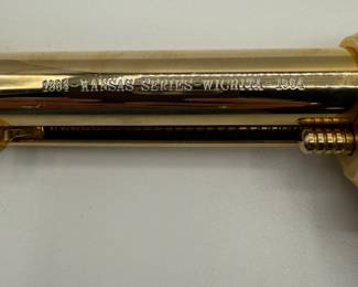 A gold-plated .22 Colt Collectible revolver featuring a pearl-colored grip. The gun has a shiny, metallic finish with a distinct shape, showcasing ornate detailing. Engraved text on the barrel reads '1864-1964 KANSAS SERIES WICHITA-1984.' The grip has a gold emblem and the overall design is a classic revolver style.