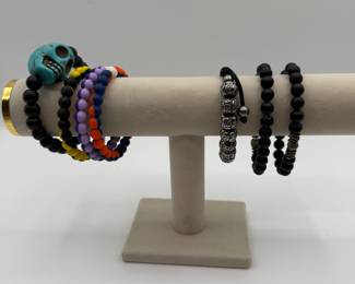 Set of colorful beaded bracelets featuring a turquoise skull accent, vibrant multi-colored beads in multiple arrangements, and black stretch bracelets with metallic and smooth accents.
