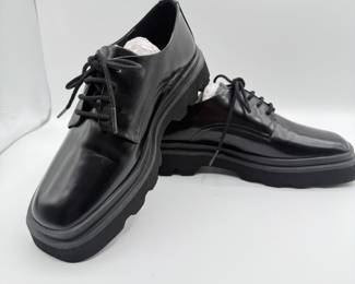 Anthropologie Chunky Black Oxfords. Anthropologie and made from shiny leather, featuring a rounded toe and traditional laces. The dress shoes have a thick black sole with a slightly elevated platform design.